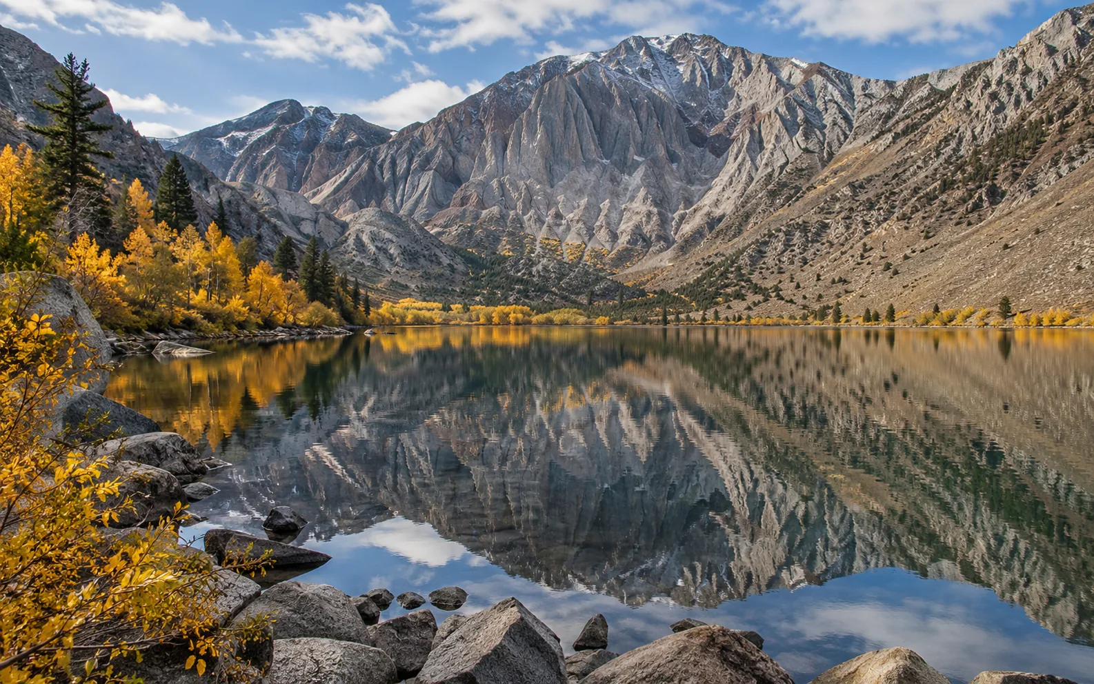 Golden aspens reflected in Convict Lake below a dramatic rock wall